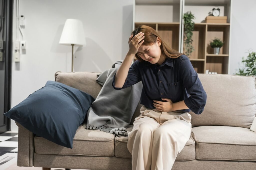 A young female Asian is resting on a sofa, experiencing menstrual cramps. She has pelvic pain, lower