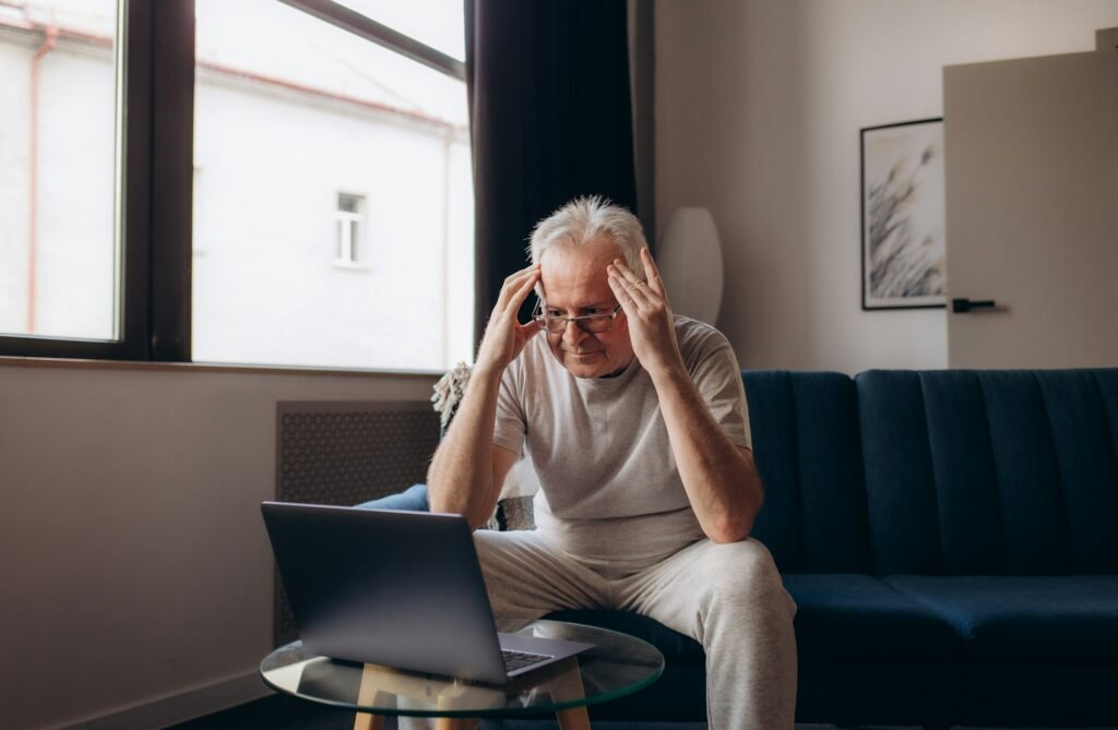 Senior man having headache and touching his head while suffering from a migraine in the living room,